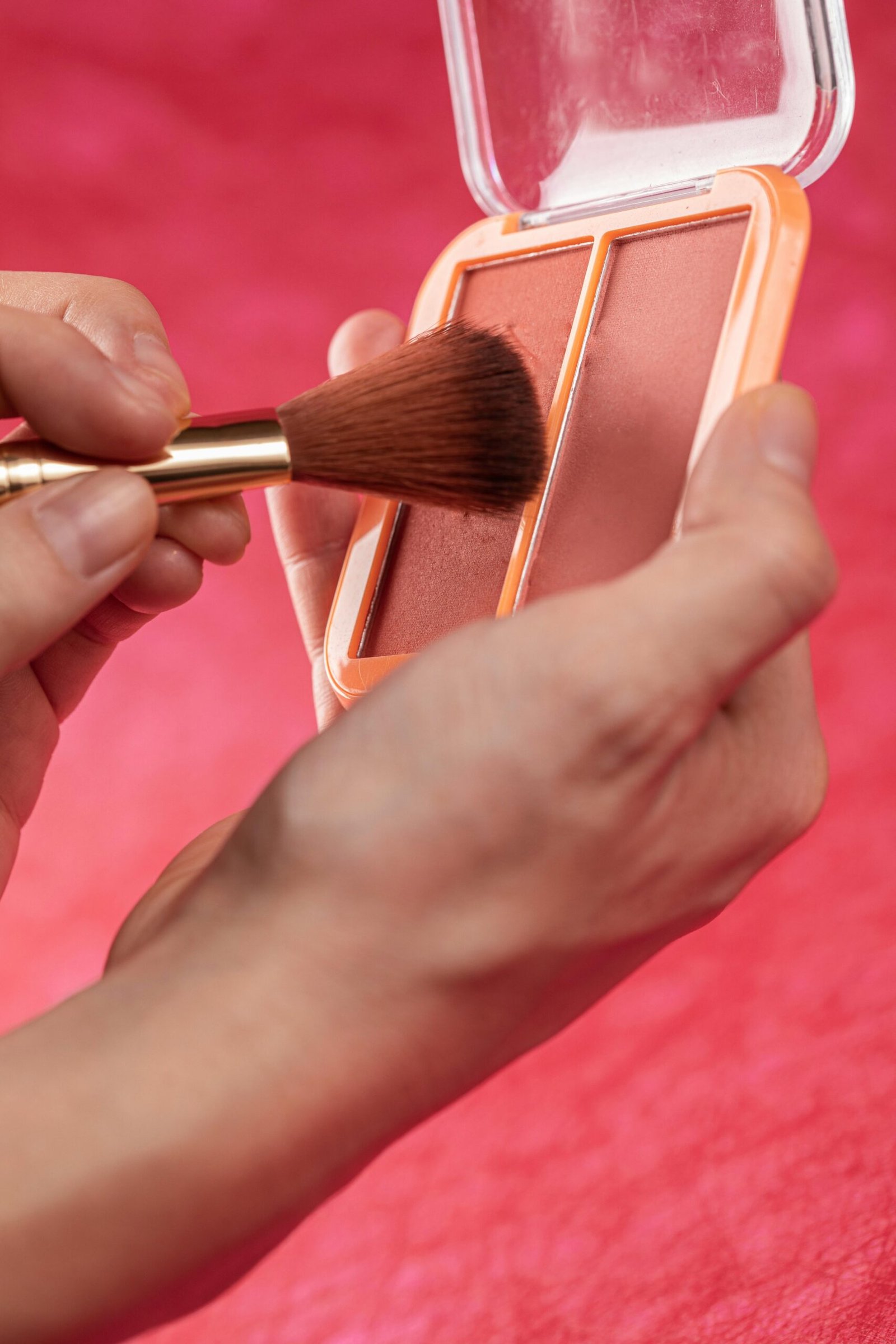 Detailed close-up of hands holding a blush palette, applying with a makeup brush.